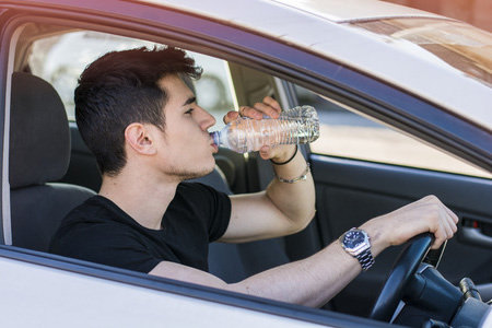 image of a person drinking bottled water whilst driving