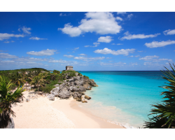 white sand beach with ruins on hill in the distance