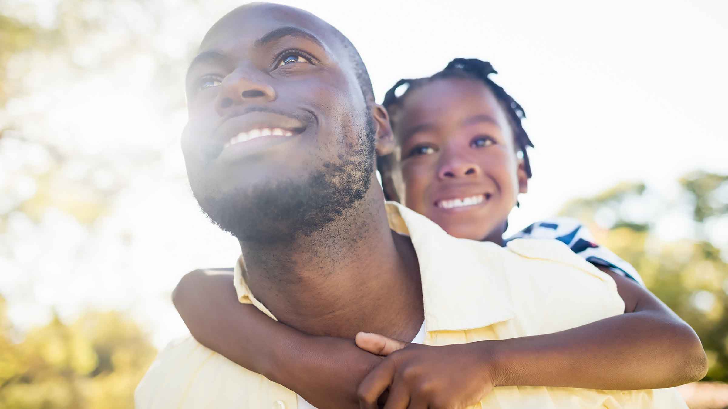 Father and child embrace and look towards sun