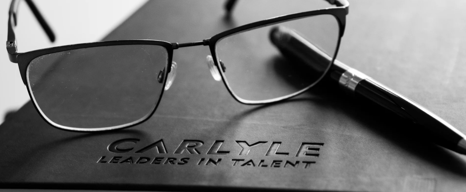 A black Carlyle notebook with a pair of glasses and a pen placed on top.