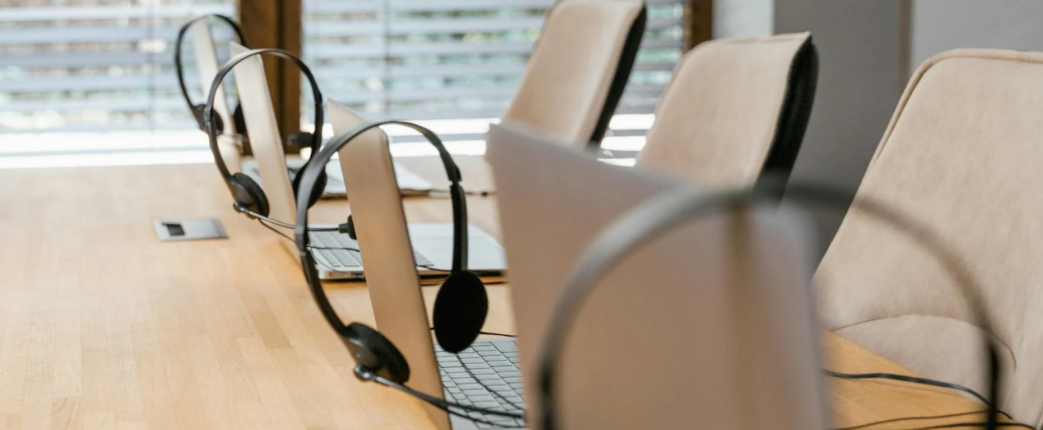 Laptops and headphones are arranged on a table in front of cream chairs.