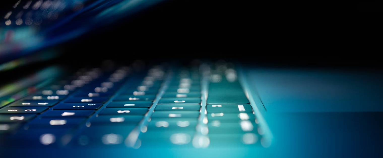 A laptop screen is half closed and the keyboard is illuminated.