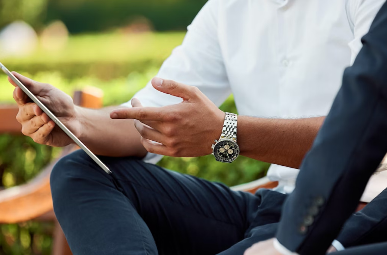 A man wearing a white shirt is sitting on a bench while pointing to a tablet.