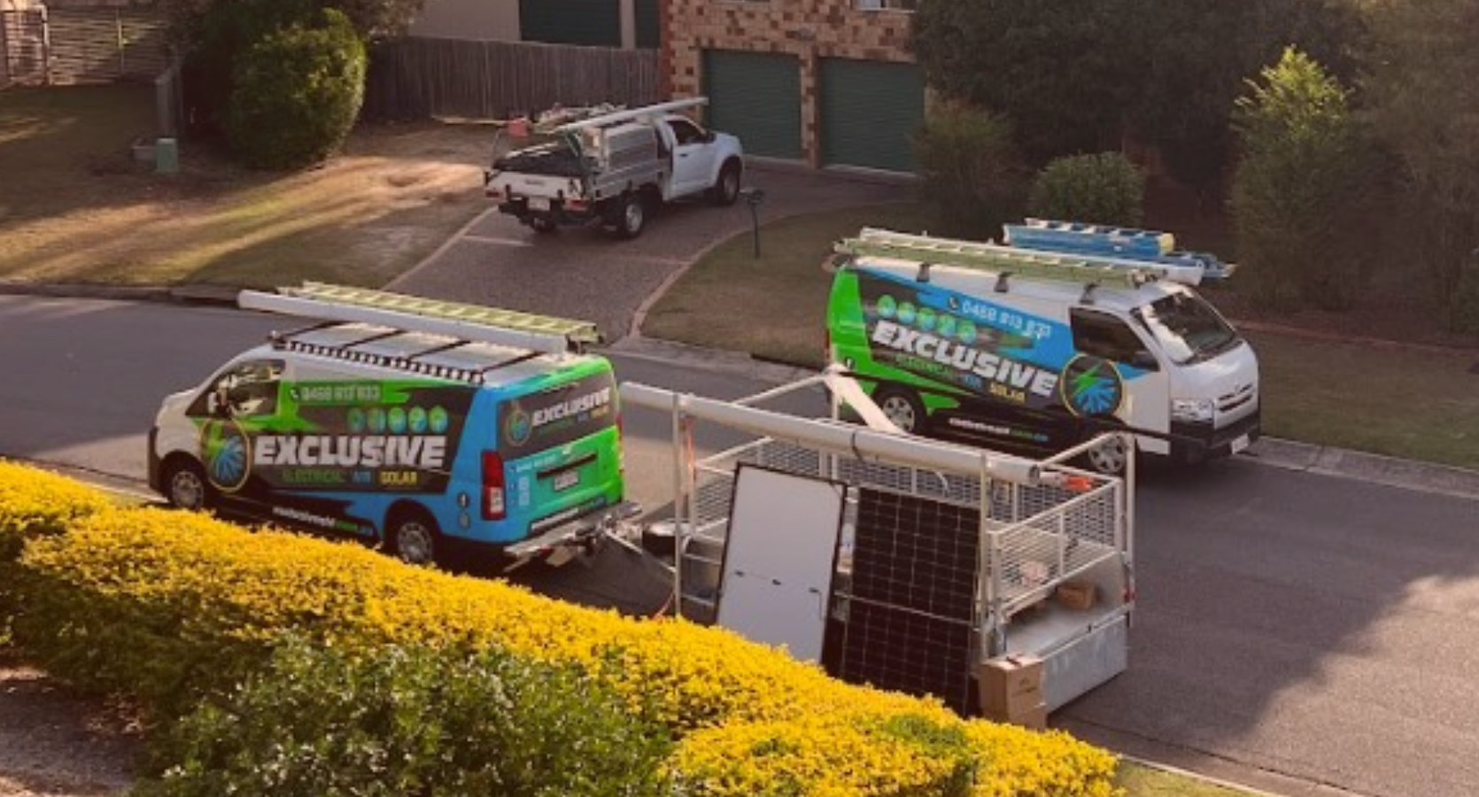 Exclusive Electrical & Air service vehicles parked in a Brisbane residential street, equipped with ladders and solar panels for installation.