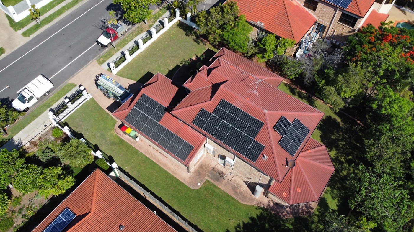 Aerial view of a Brisbane home with extensive solar panel installation on a red tiled roof, completed by Exclusive Electrical & Air for sustainable energy efficiency.