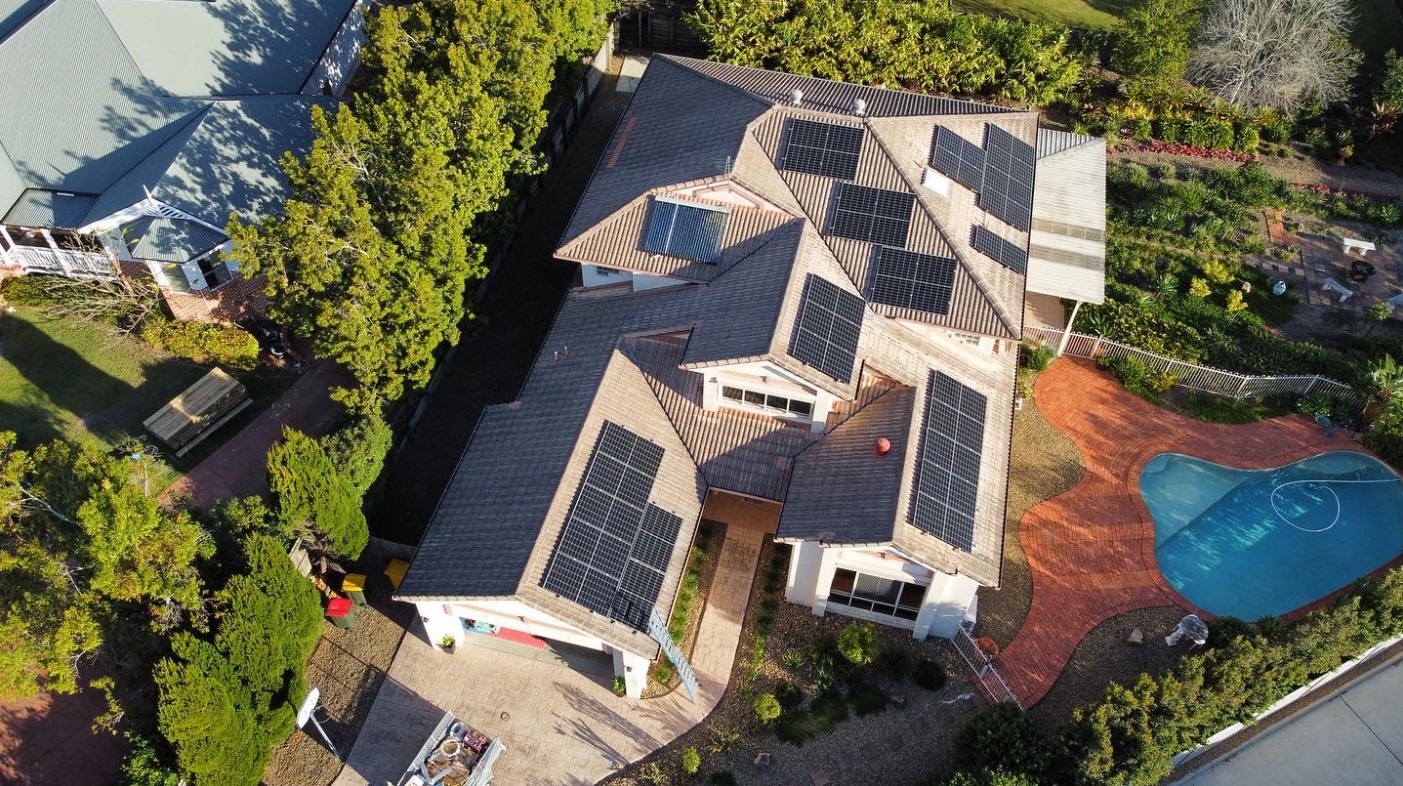 Aerial view of a Brisbane home with multiple solar panel arrays installed on a tiled roof, completed by Exclusive Electrical & Air, featuring a landscaped backyard and swimming pool.