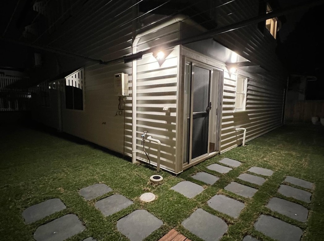 Night view of a Brisbane home with outdoor wall lights installed by Exclusive Electrical & Air, illuminating the backyard entrance and pathway with a clean, modern finish.