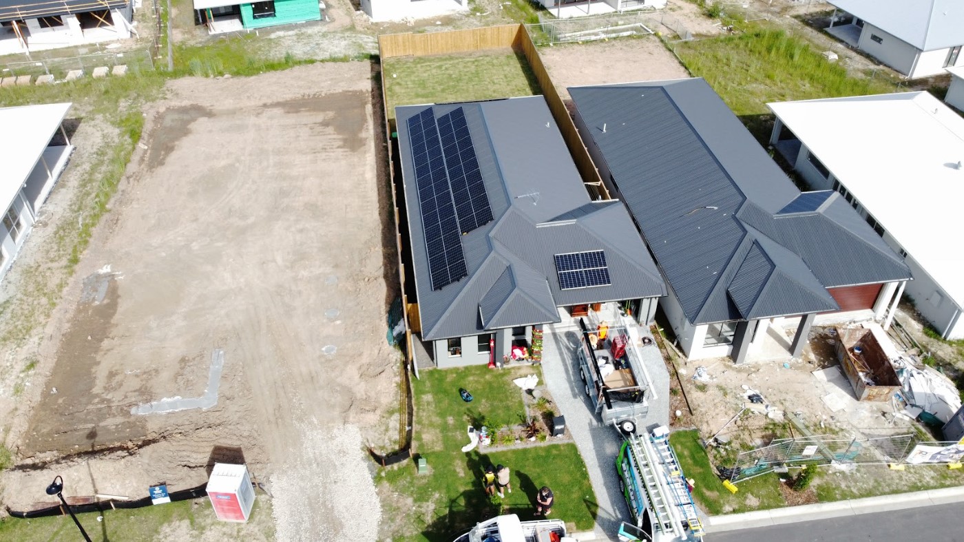 Aerial view of a modern home with freshly installed solar panels on a dark roof, part of a new housing development in Brisbane.