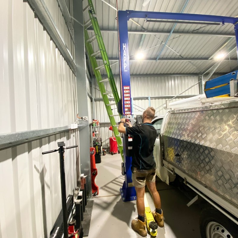 Electrician from Exclusive Electrical & Air working on a vehicle hoist installation in a modern workshop, ensuring safe and compliant electrical setup.