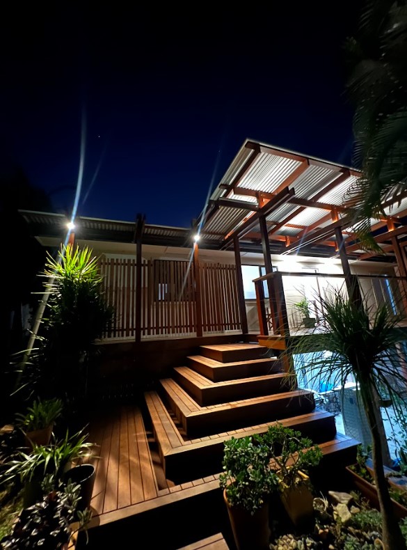 A beautifully illuminated wooden staircase and patio with modern outdoor step lighting installed by Exclusive Electrical & Air, enhancing both safety and aesthetic appeal at night.