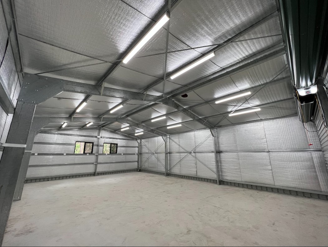 Brightly lit industrial shed interior featuring multiple energy-efficient LED batten lights installed on the ceiling. The clean, modern setup highlights reflective insulation and durable steel framing, providing excellent illumination for a functional workspace.