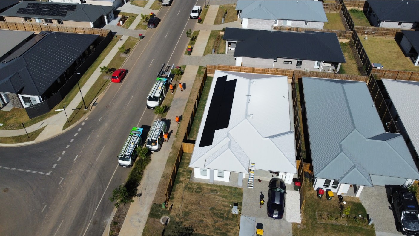 Aerial view of a new home with sleek black solar panels installed on a white roof, with Exclusive Electrical & Air service vehicles and team members working on-site.