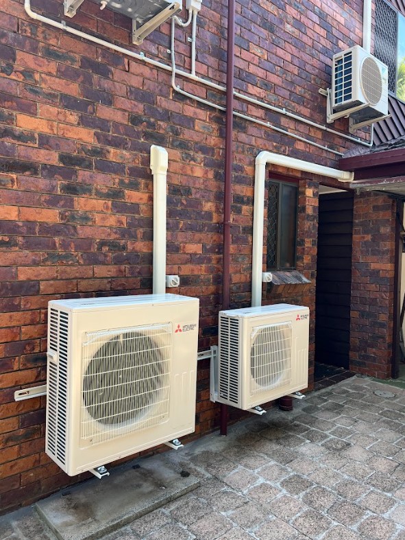 Two Mitsubishi Electric outdoor air conditioning units mounted on a brick wall with professional piping and wiring, part of a residential cooling installation.