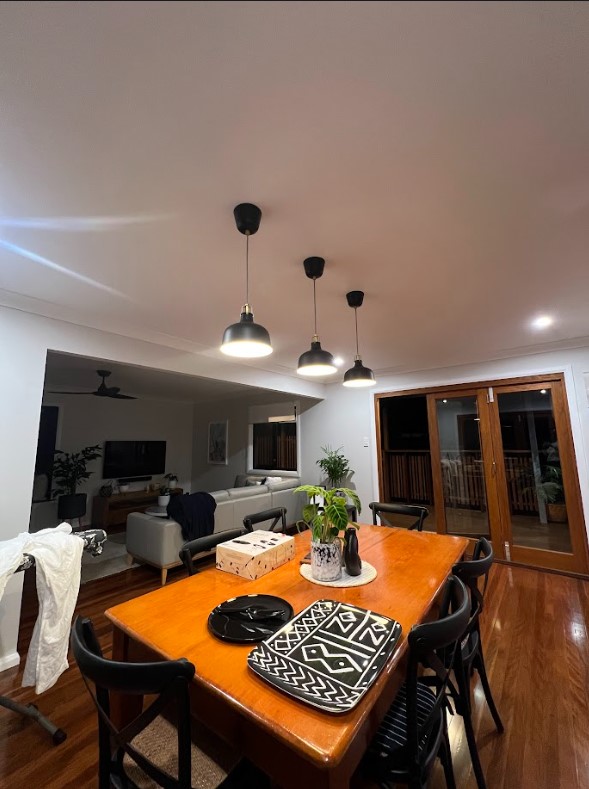 Exclusive Electrical & Air installed stylish pendant lighting in a dining room with a timber table and black chairs, enhancing the open-plan living space with a modern and energy-efficient lighting design.