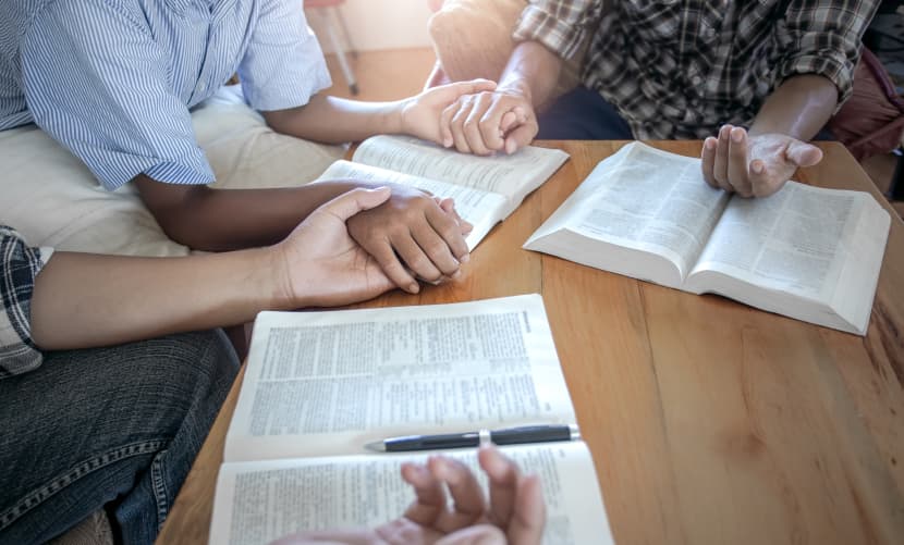 Christian group praying together around wooden table with open b