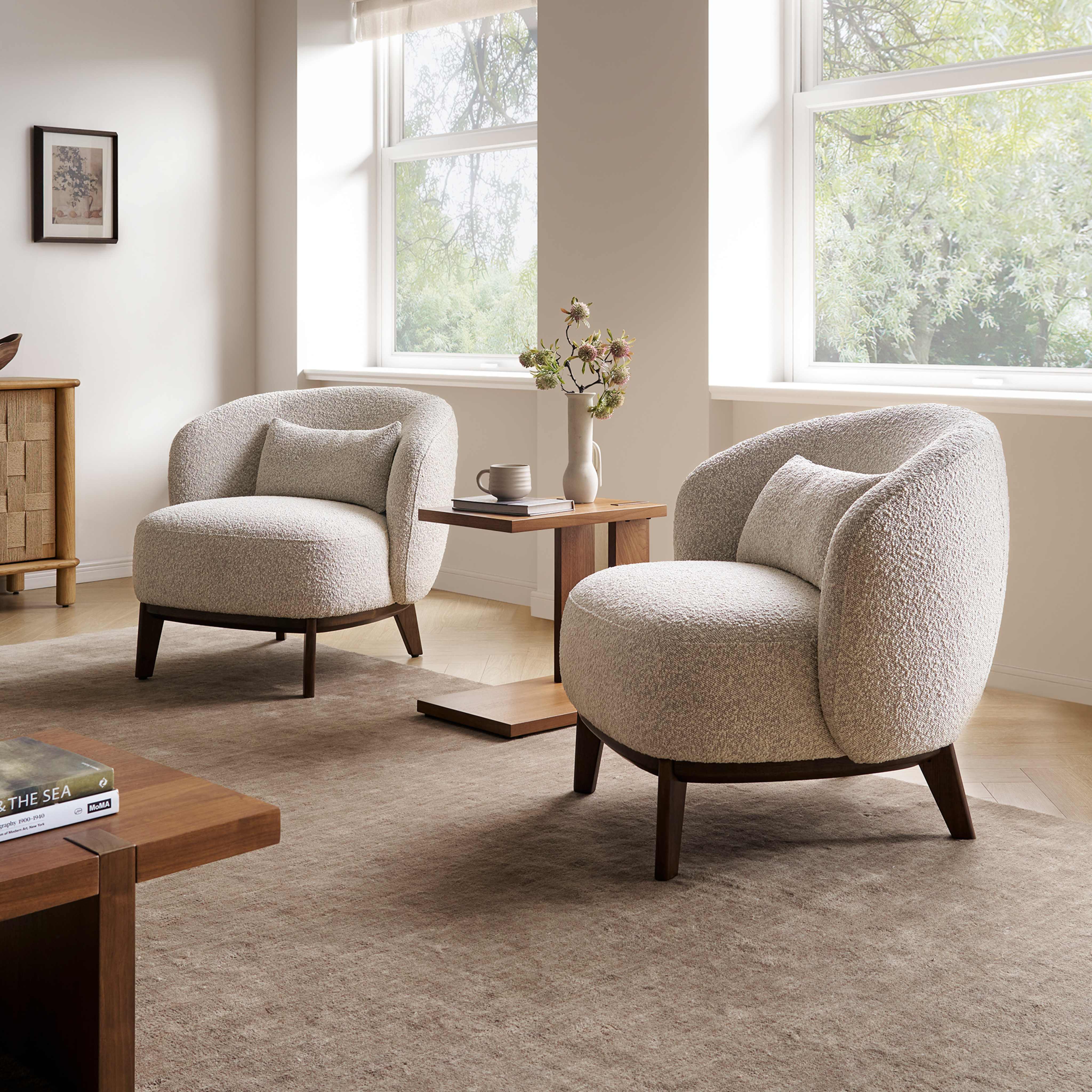 Two bouclé armchairs and a side table in a living room.