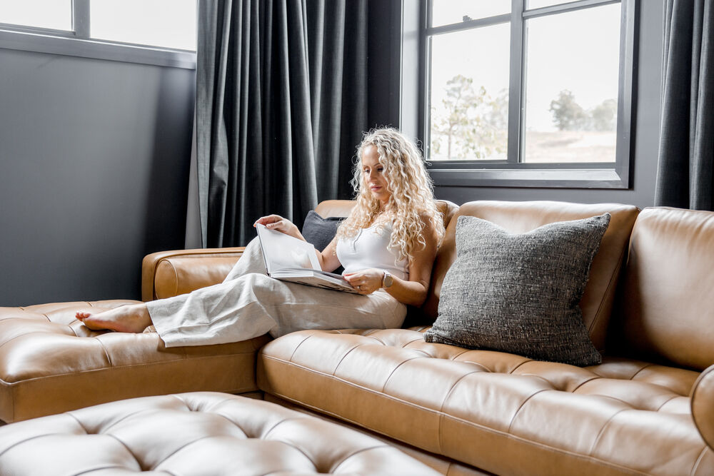 A person reading a book on a leather chaise sectional sofa.