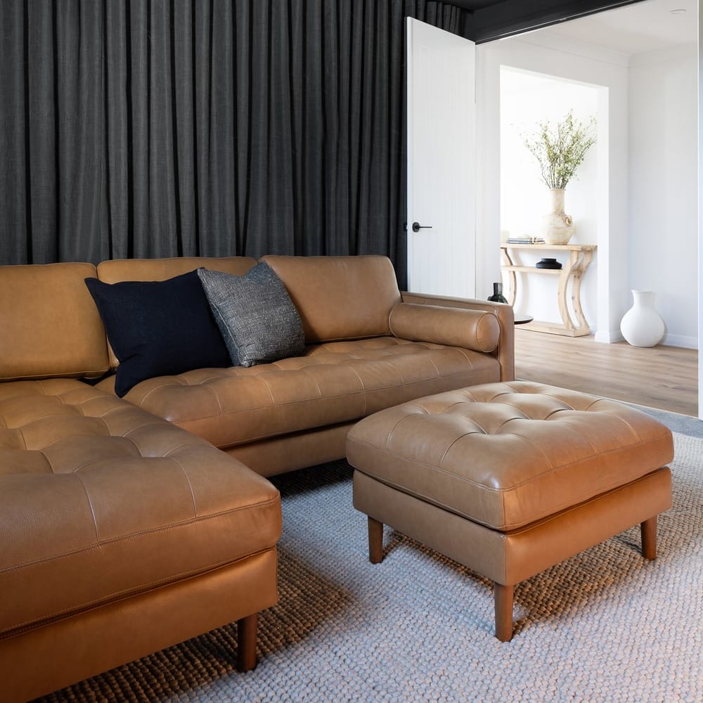 A leather chaise sectional sofa with a matching ottoman and two cushions.