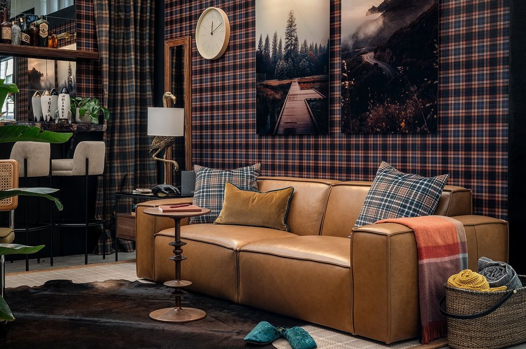 A leather sofa in a living room with checkered wallpaper and throw cushions.