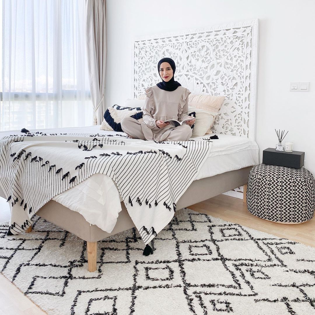 A person sitting on a bed with a tall patterned headboard.