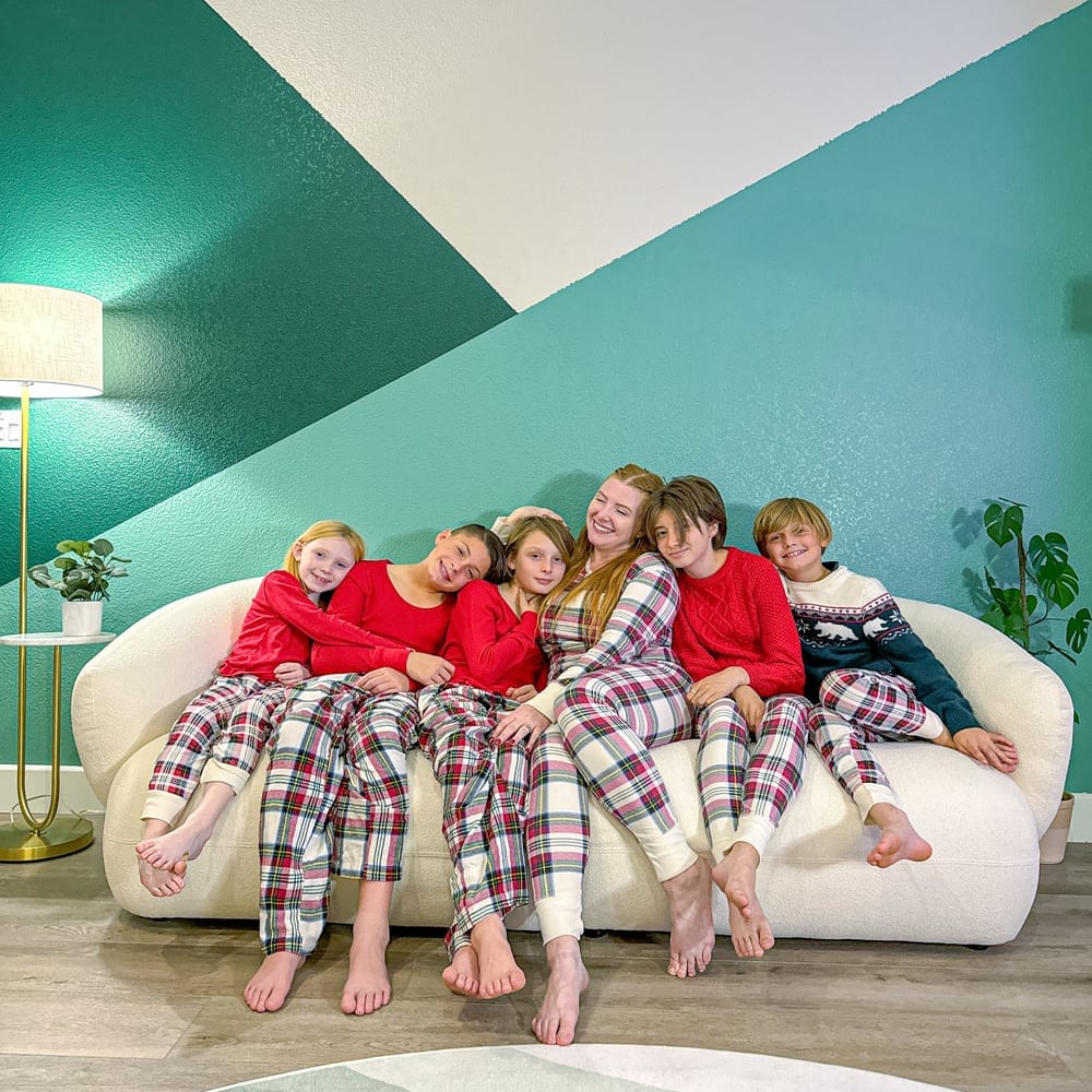 6 people sitting on a white sofa against a green patterned wall.