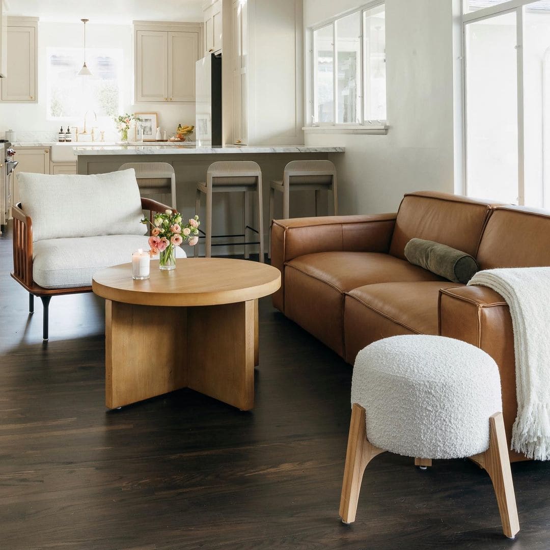 A leather 2-seater sofa, a wooden armchair, and a bouclé stool surrounding a round wooden coffee table in the living room.