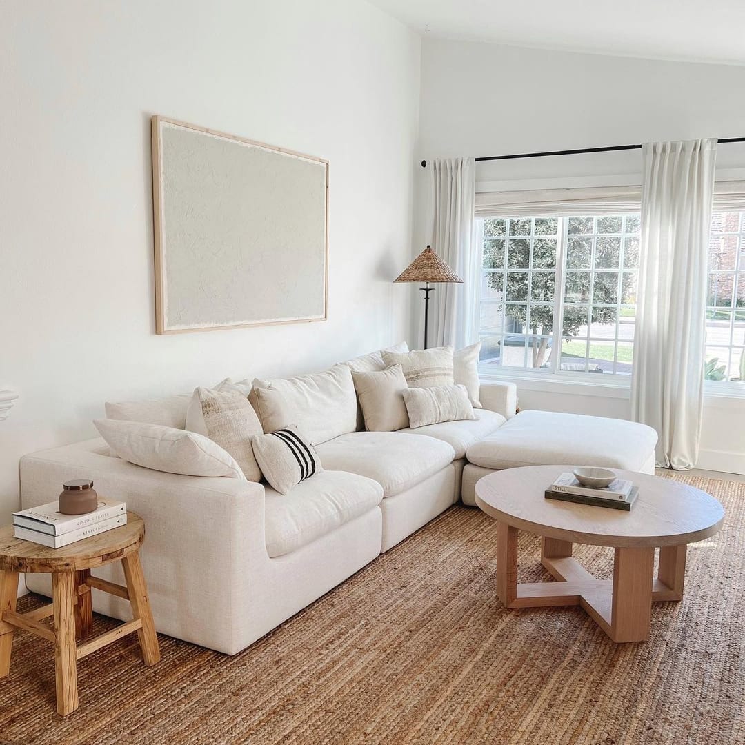 A white sectional sofa, a side table, and round coffee table placed atop a large area rug.