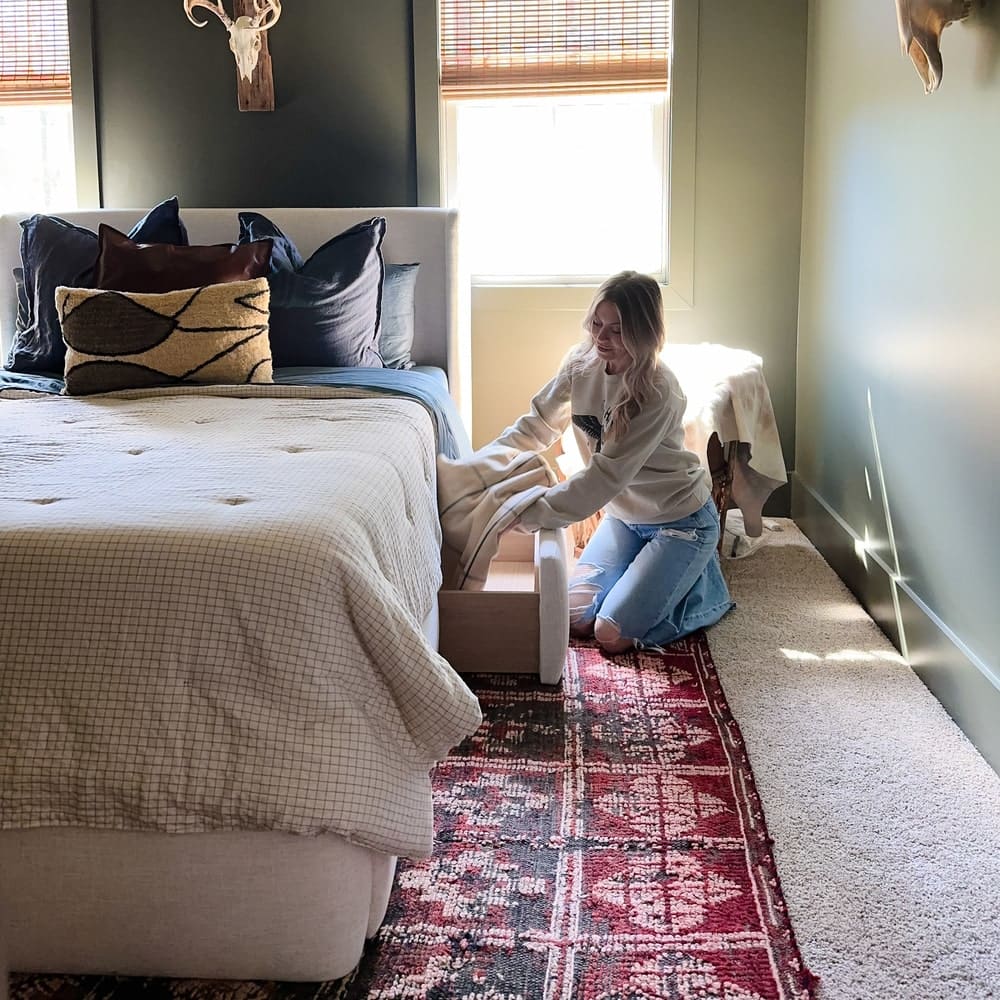 A person storing bedding away in a pull-out drawer of a storage bed.