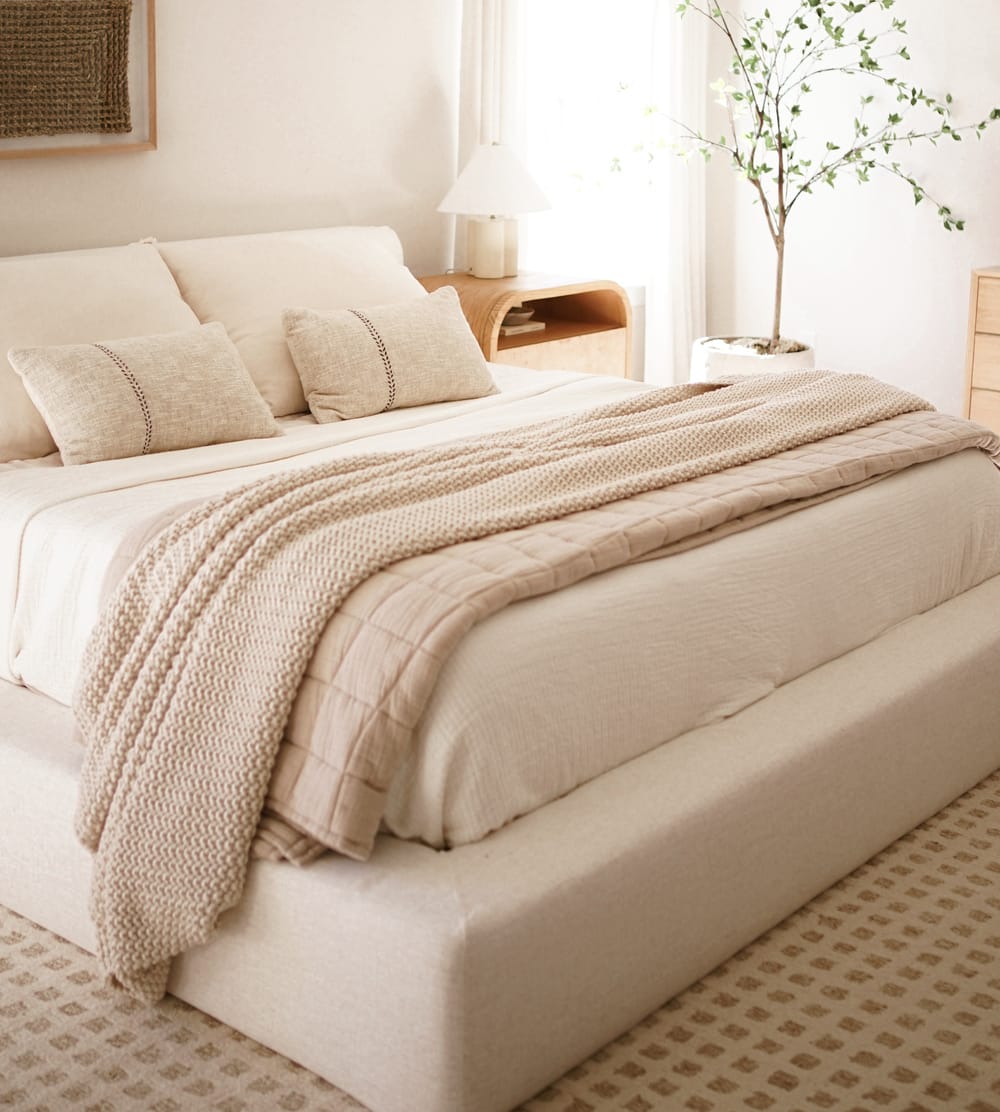 A storage bed with white bedsheets and beige throws and pillows.