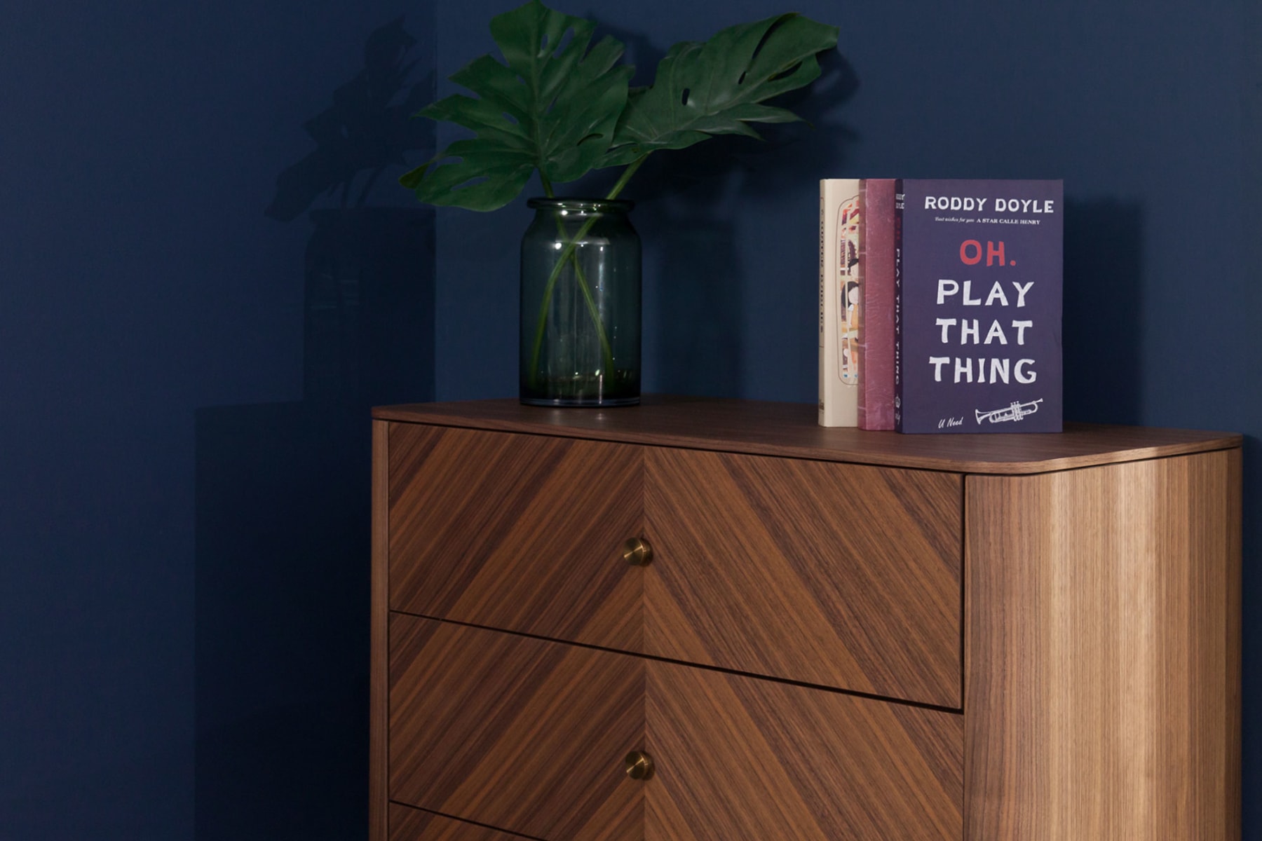 A wooden dresser is decorated with a vase and some books