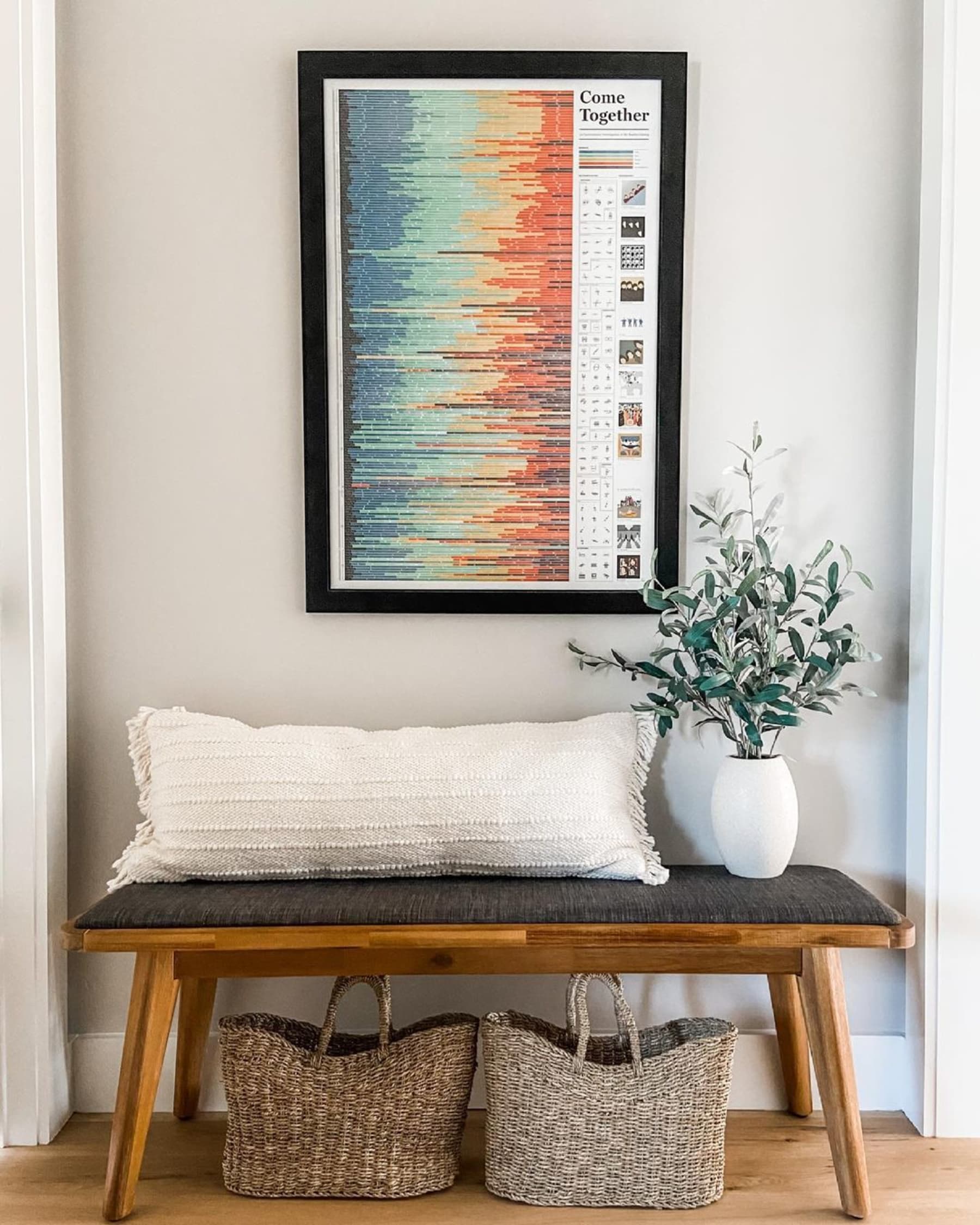 Entryway dining bench below a wall artpiece styled with lumbar cushion and a potted plant