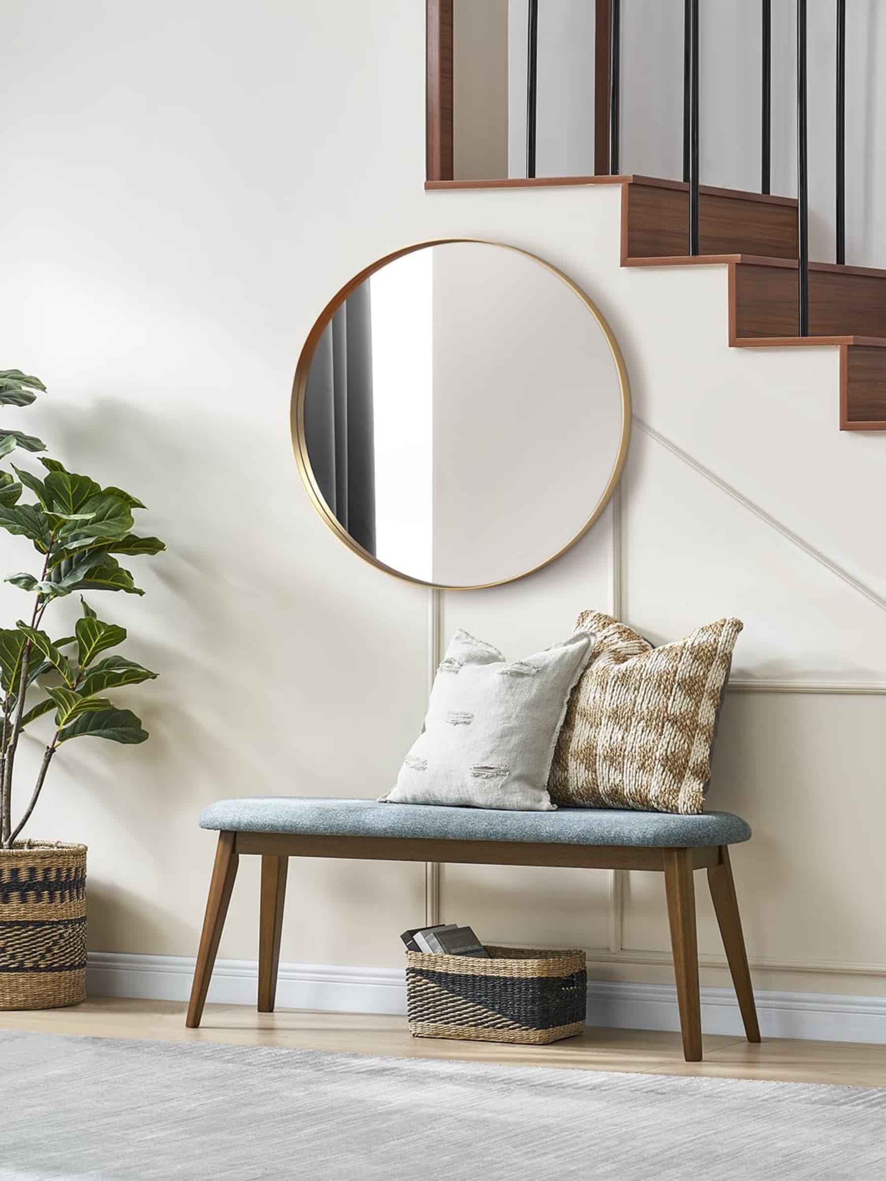 Blue upholstered entryway dining bench with dark wood legs and base, styled with a rug, cushions and a round mirror