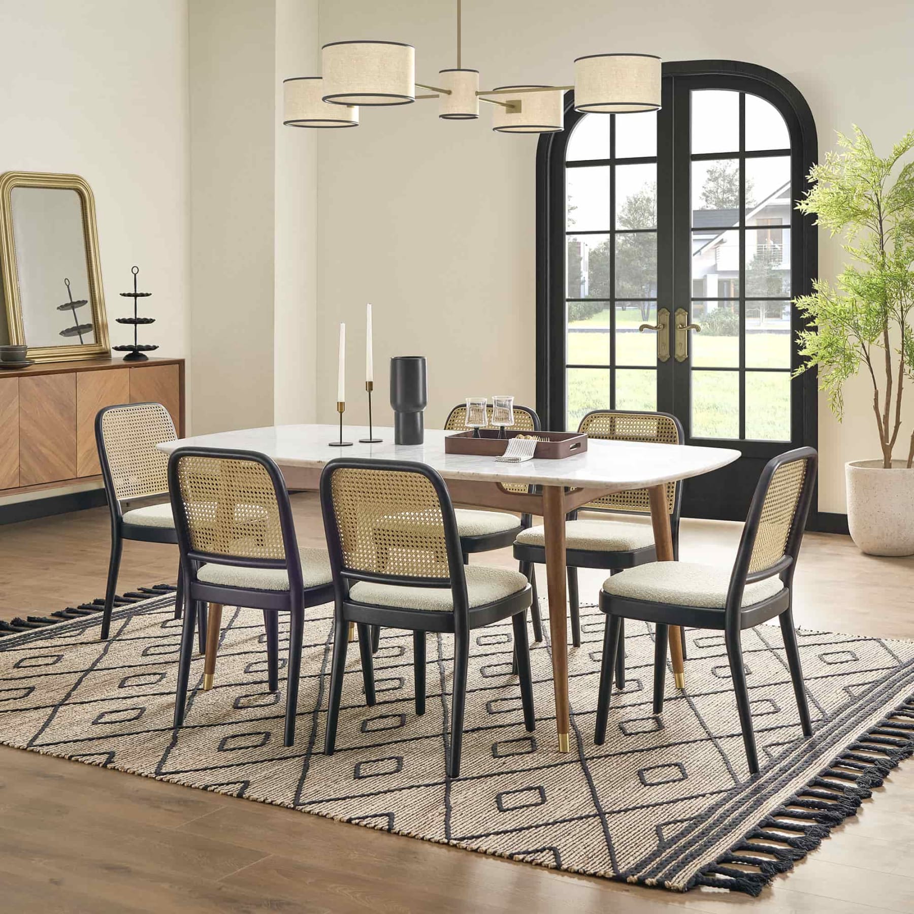 6 black cane dining chairs and a marble dining table atop a jute rug.