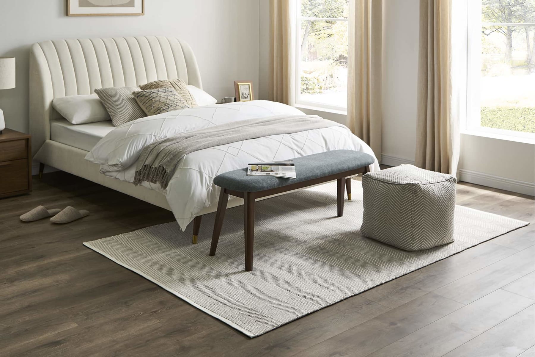 neutral beige cotton rug below a fabric and wood bench at the foot of a tufted bed