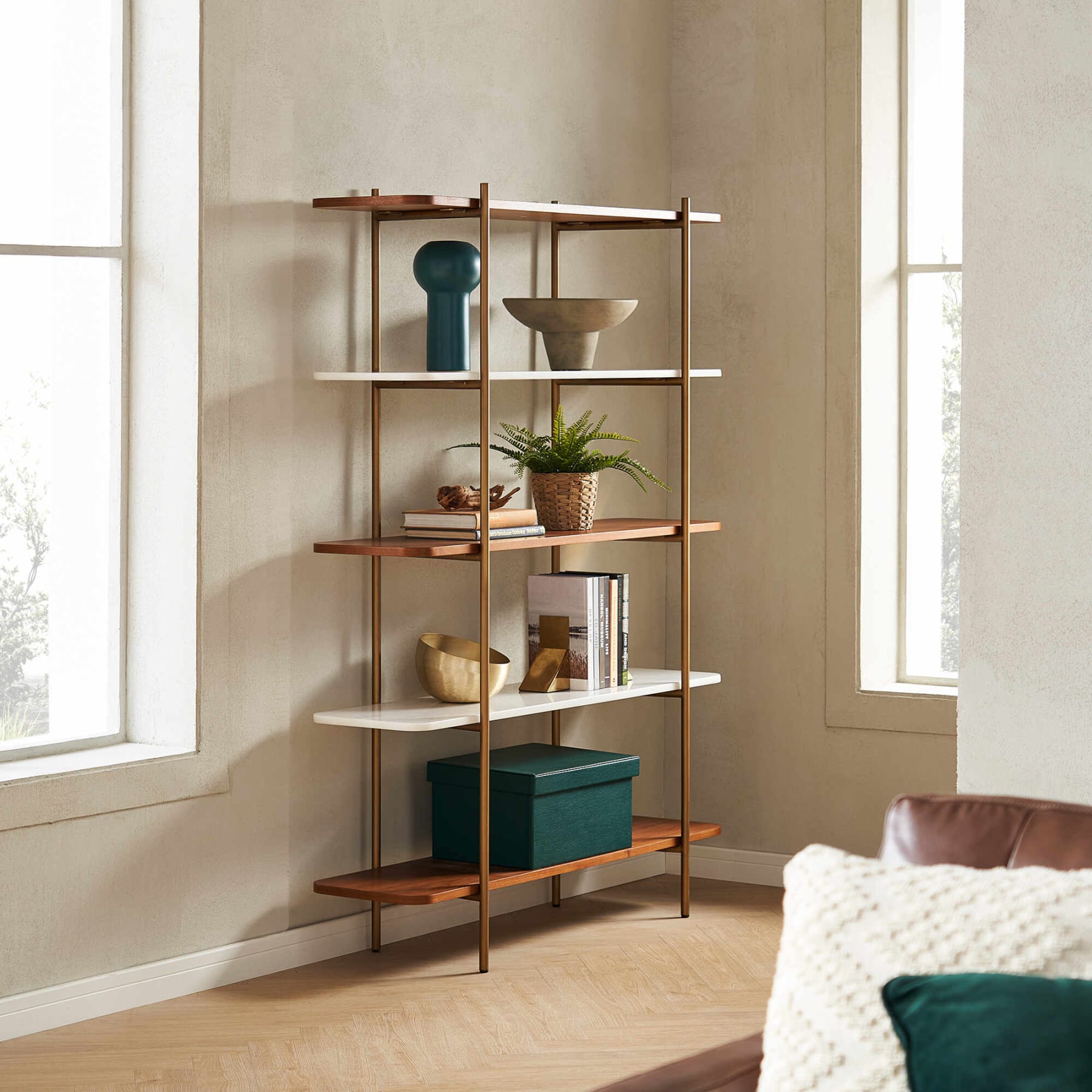 A shelf with gold metal frames asymmetrical vases, books, and a potted plant.