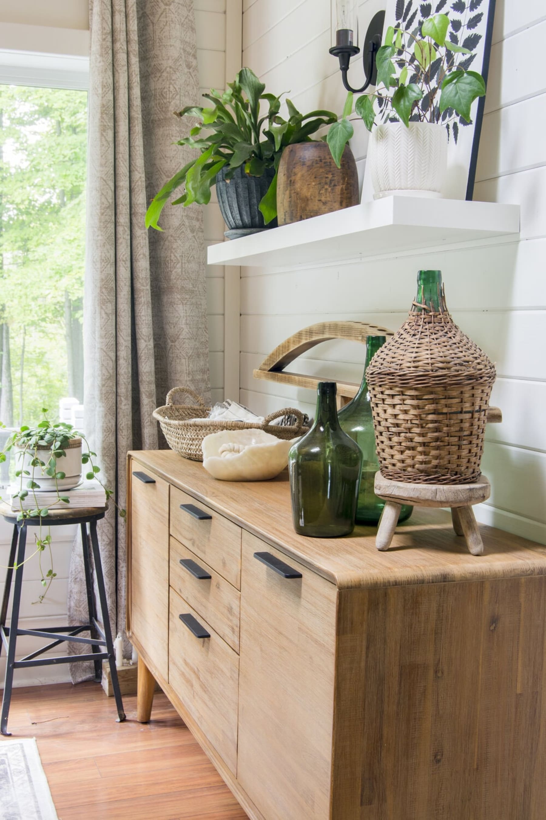 A rustic wooden sideboard with several potted plants and decorative items like glass bottles and woven baskets.