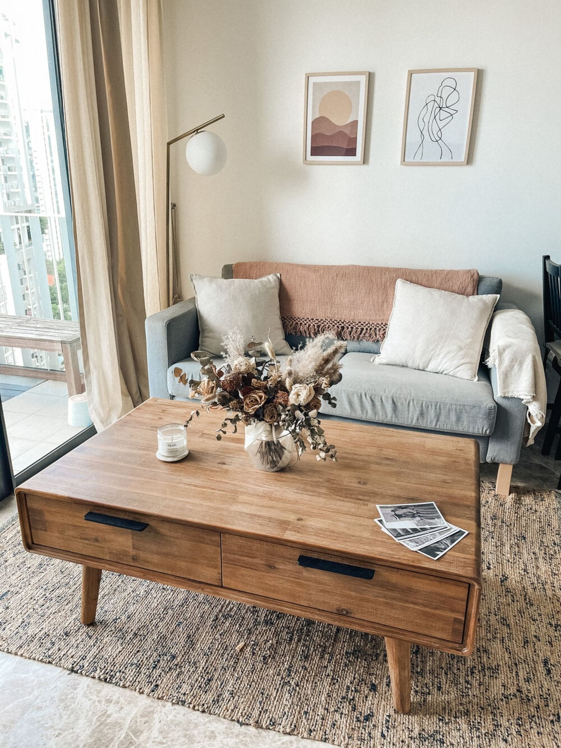 A rustic coffee table with storage has a bouquet of flowers and a candle atop.