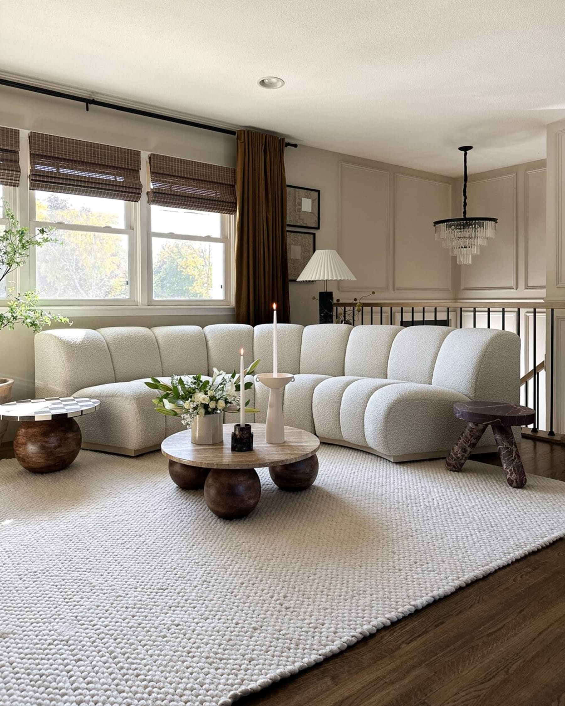 A curved bouclé sofa sits at the corner of the space and is complemented by marbled coffee tables and stools.