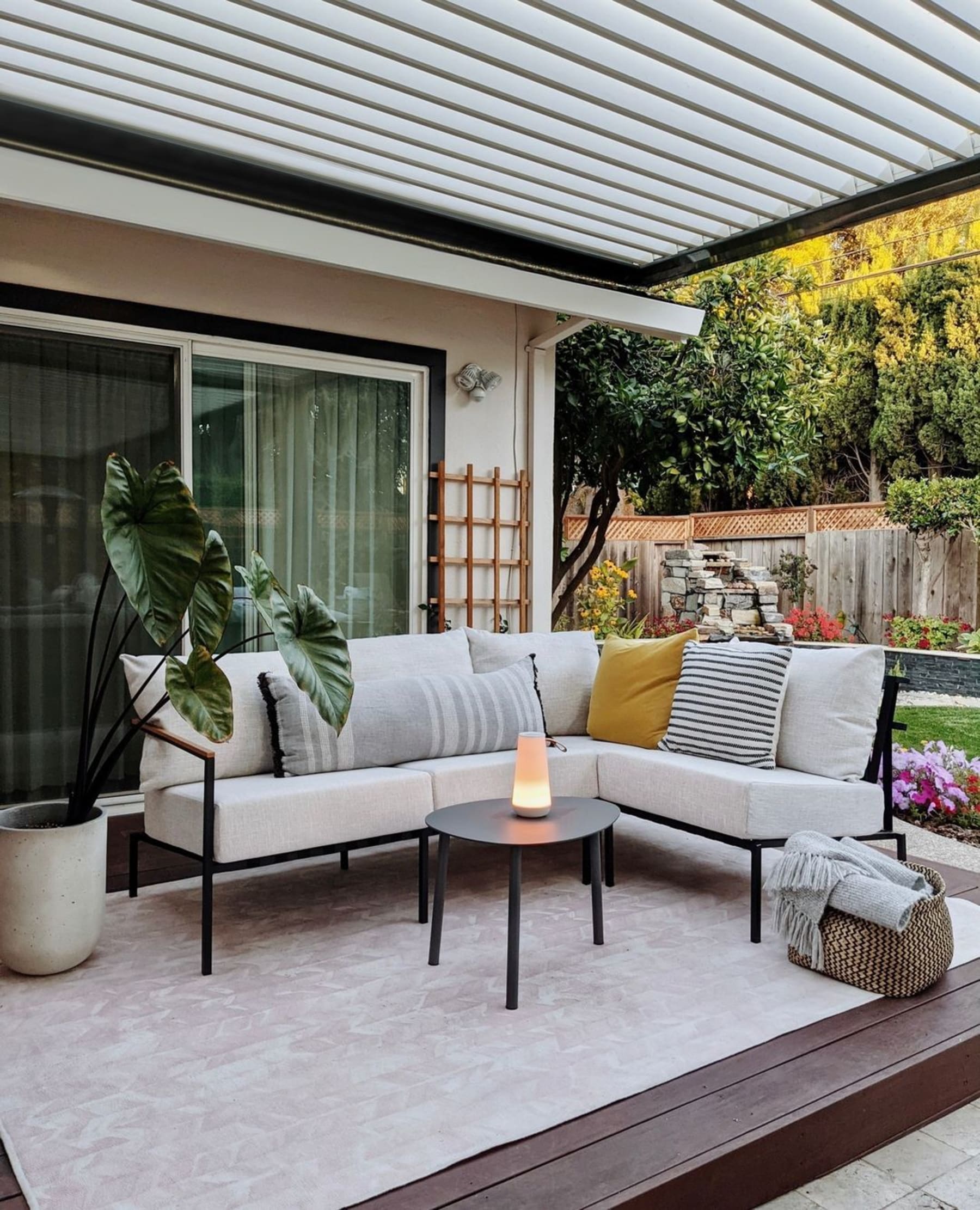 An outdoor section sofa with a black aluminum frame sits atop a wooden deck.