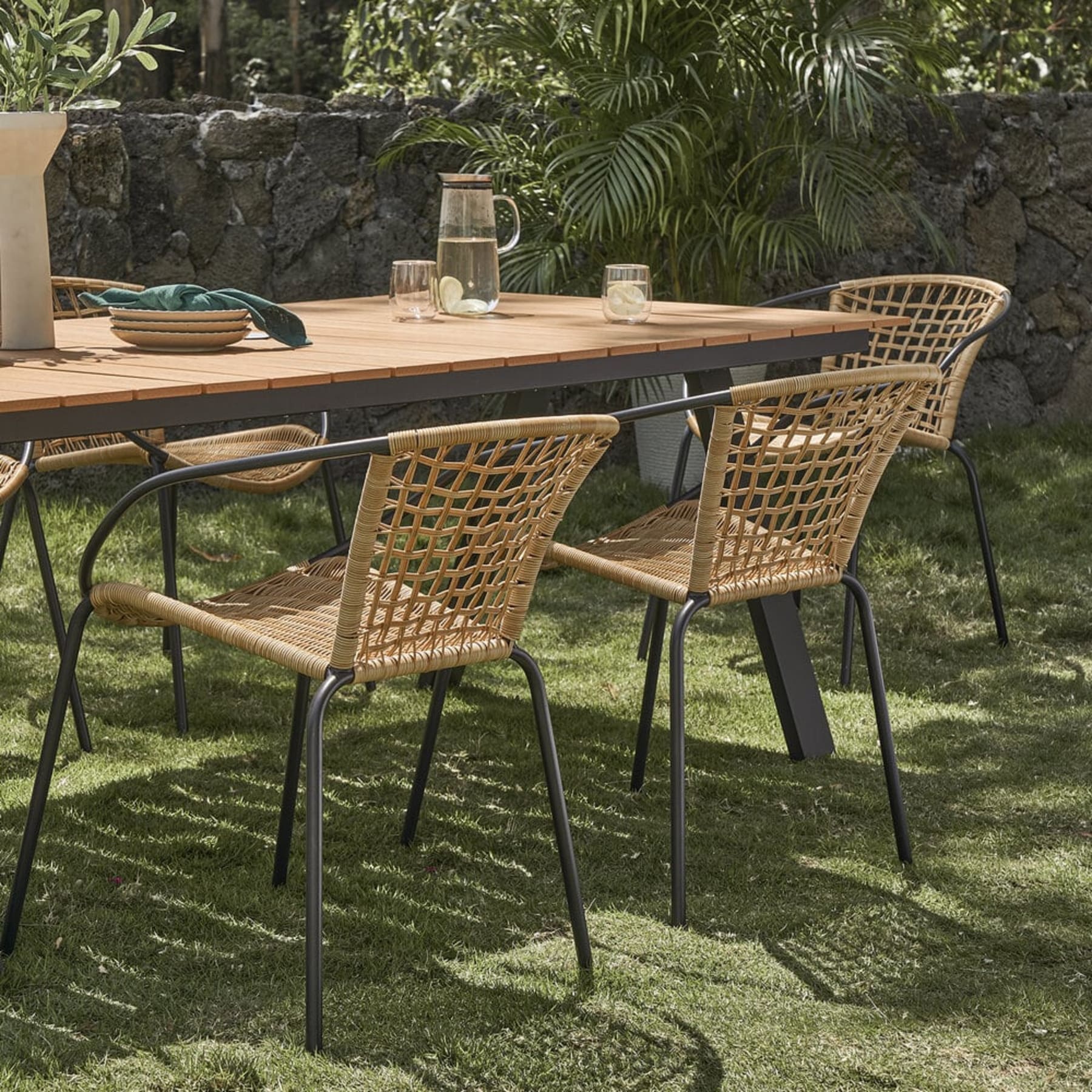 Resin wicker chairs are placed in the garden along with a wooden dining table.