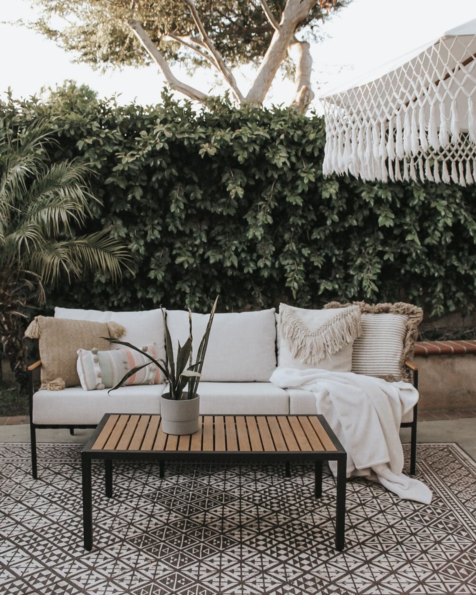 An outdoor sofa and coffee table is decorated with pillows, a throw, and a potted plant.