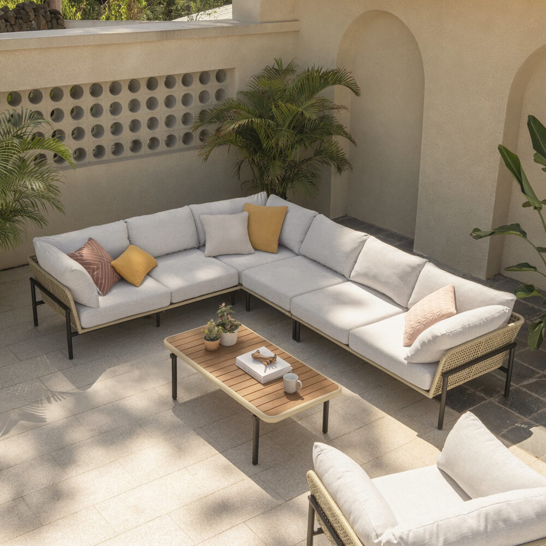 A rattan sofa, lounge chair, and wooden coffee table are placed outdoors under the shade.