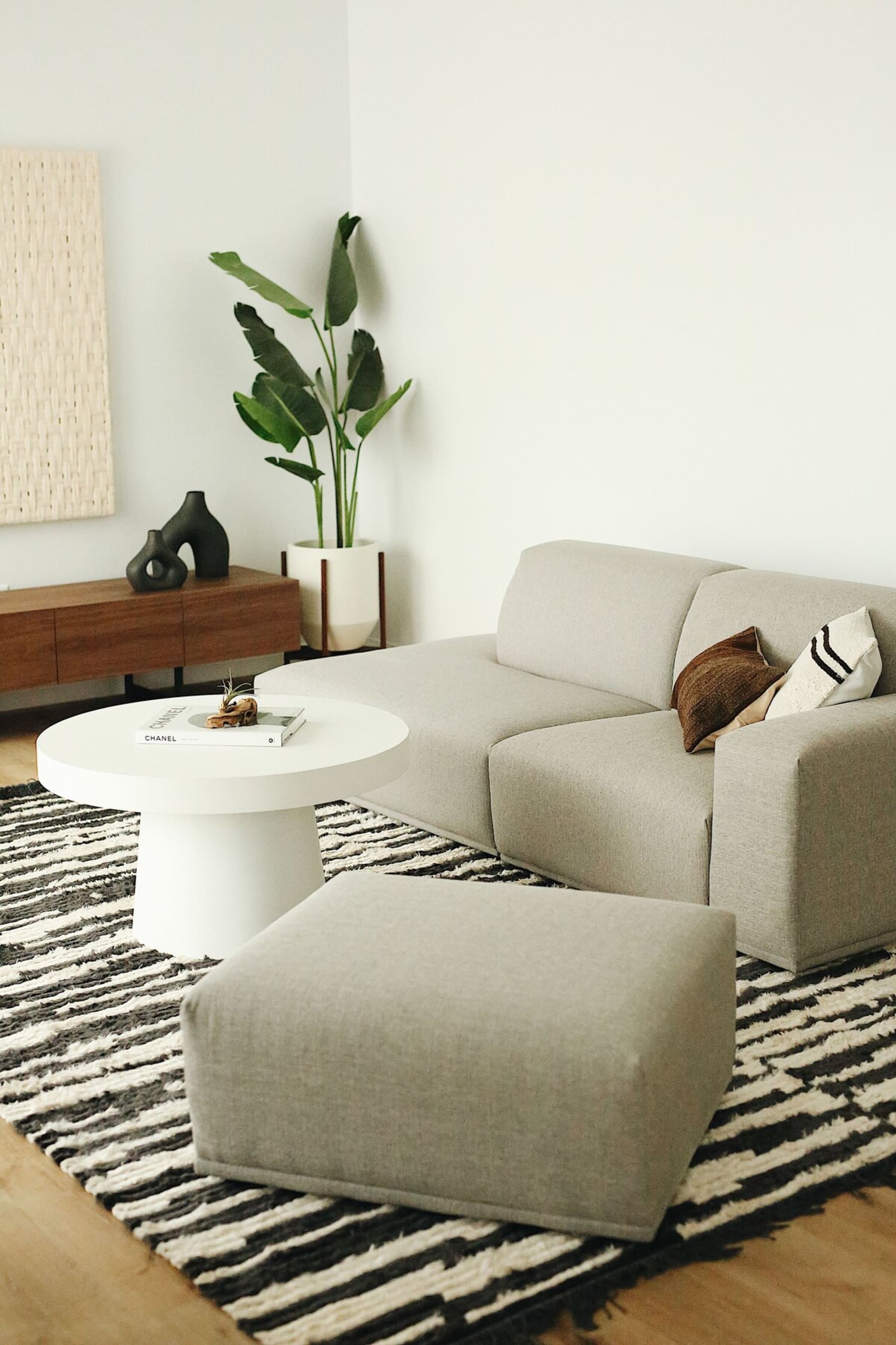 A minimalistic gray fabric sofa and matching ottoman sit on a patterned rug.