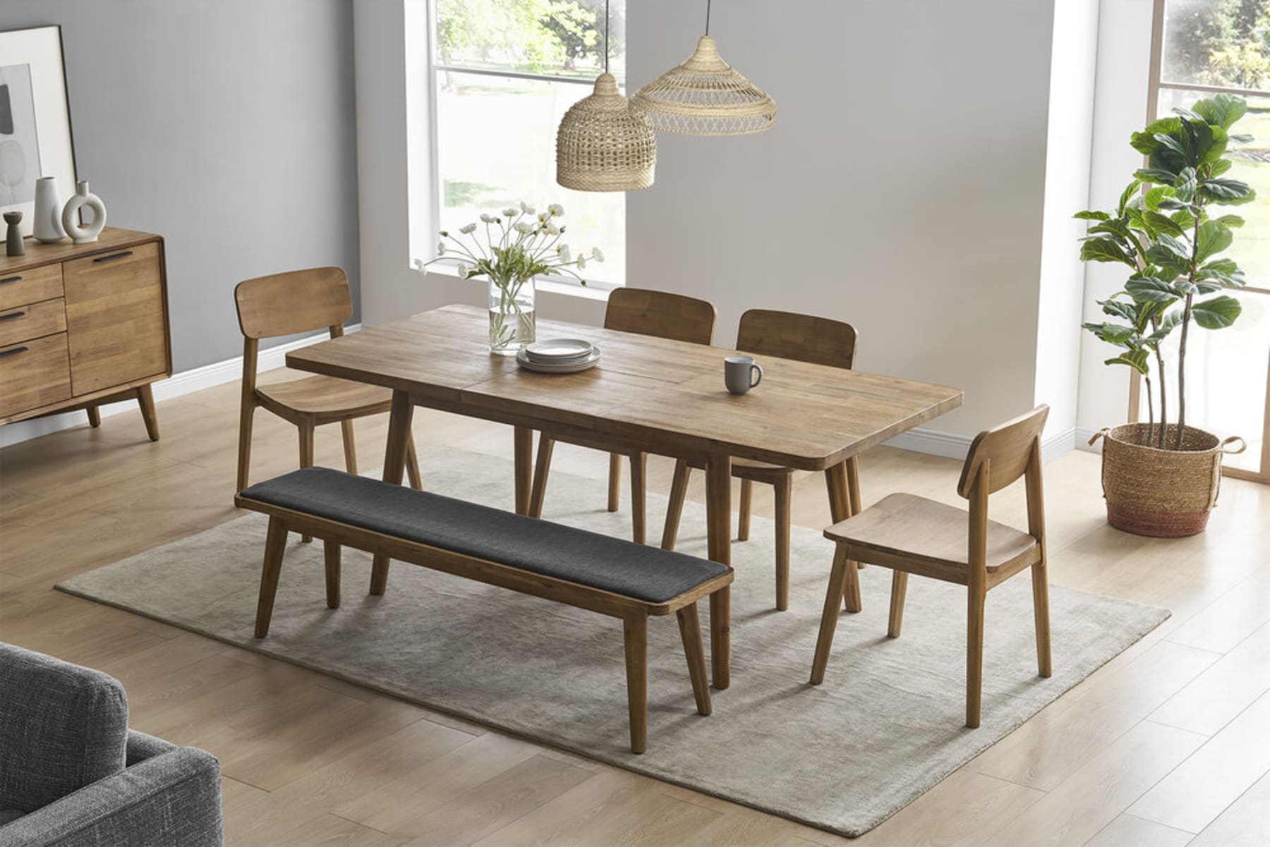 A plant in a woven basket is placed behind a matching wooden dining table set.