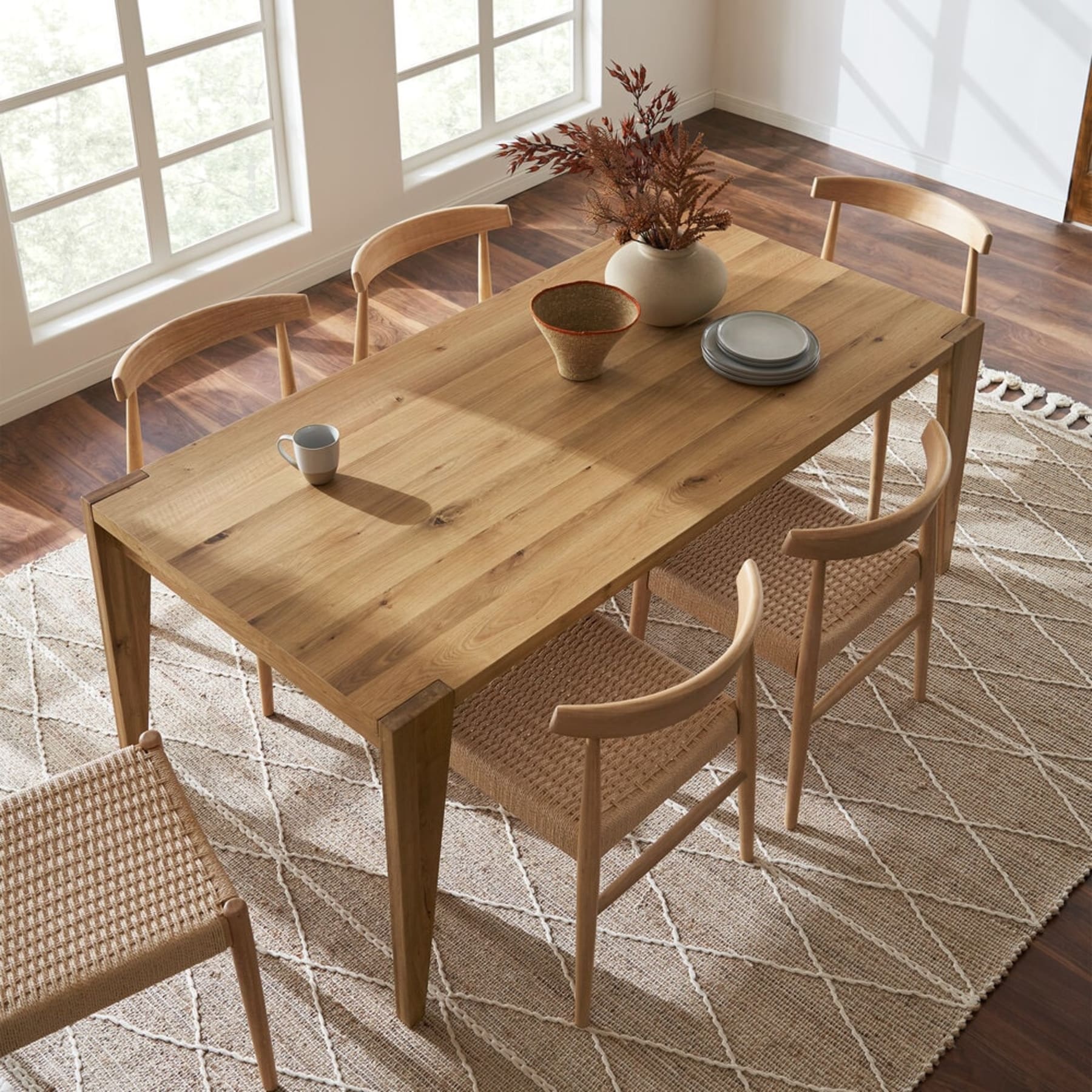 A wooden extendable dining table has tableware and a vase atop.