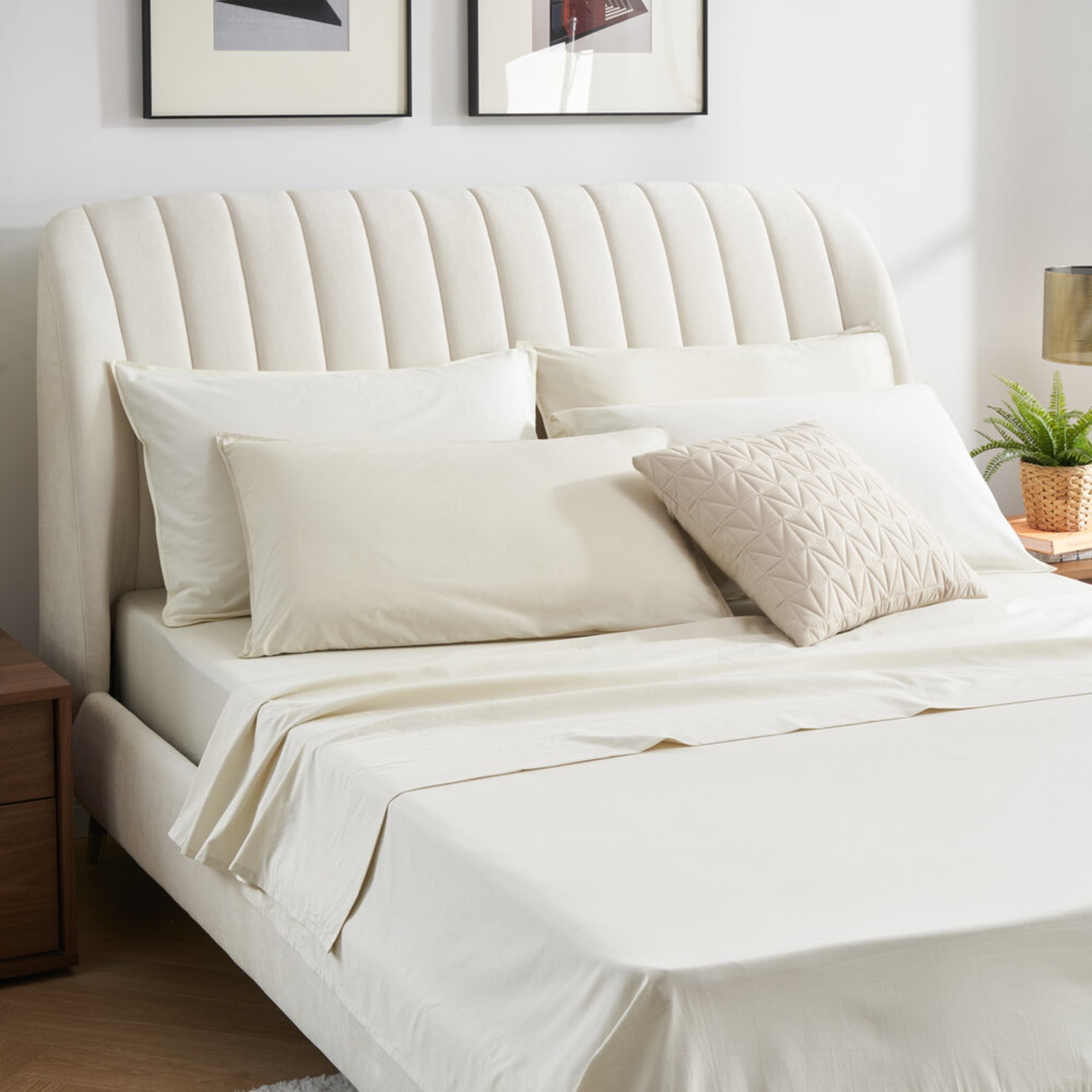 A bed with a padded headboard, pillows, and a cushion.