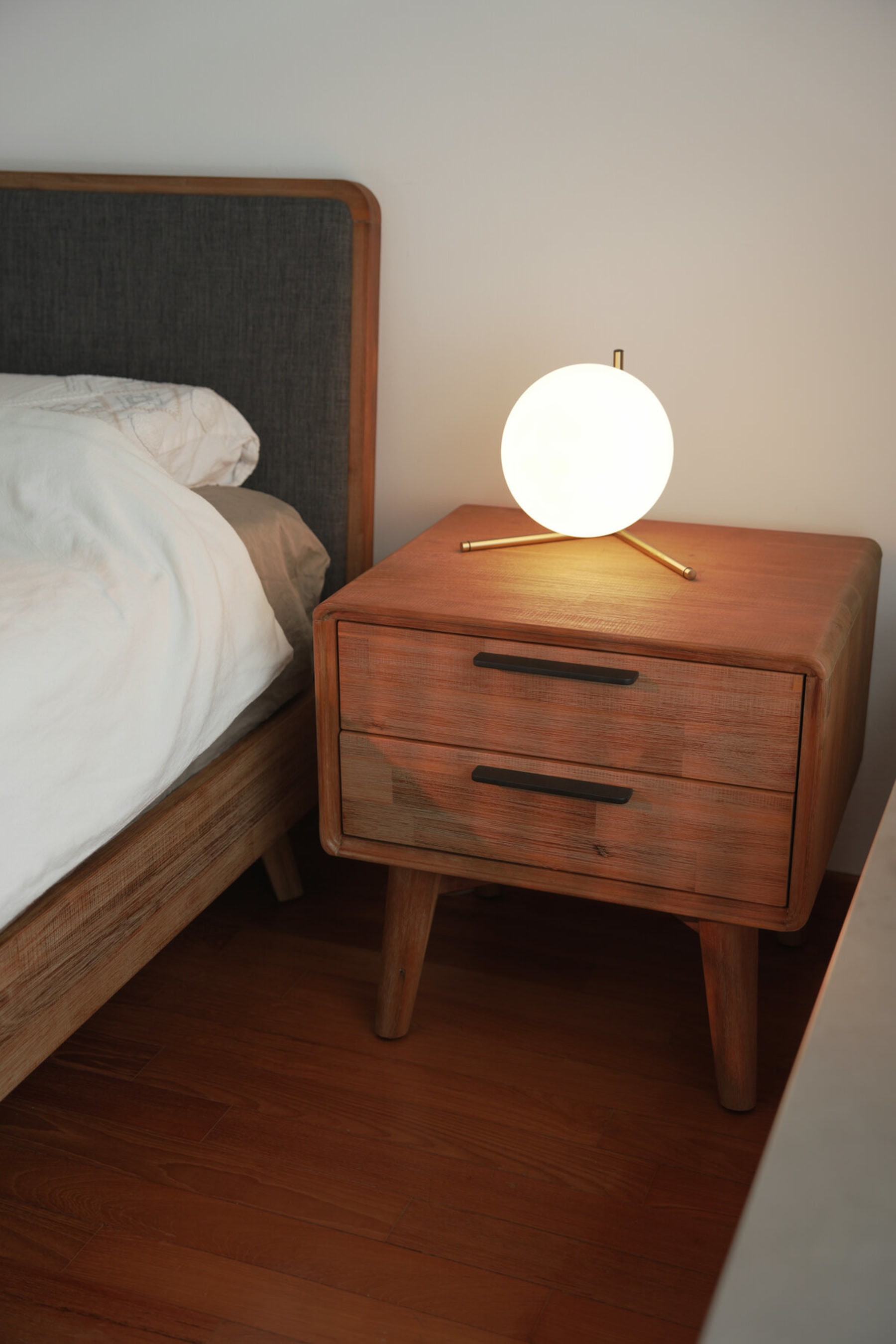 A wooden bedside table with 2 drawers with a table lamp.