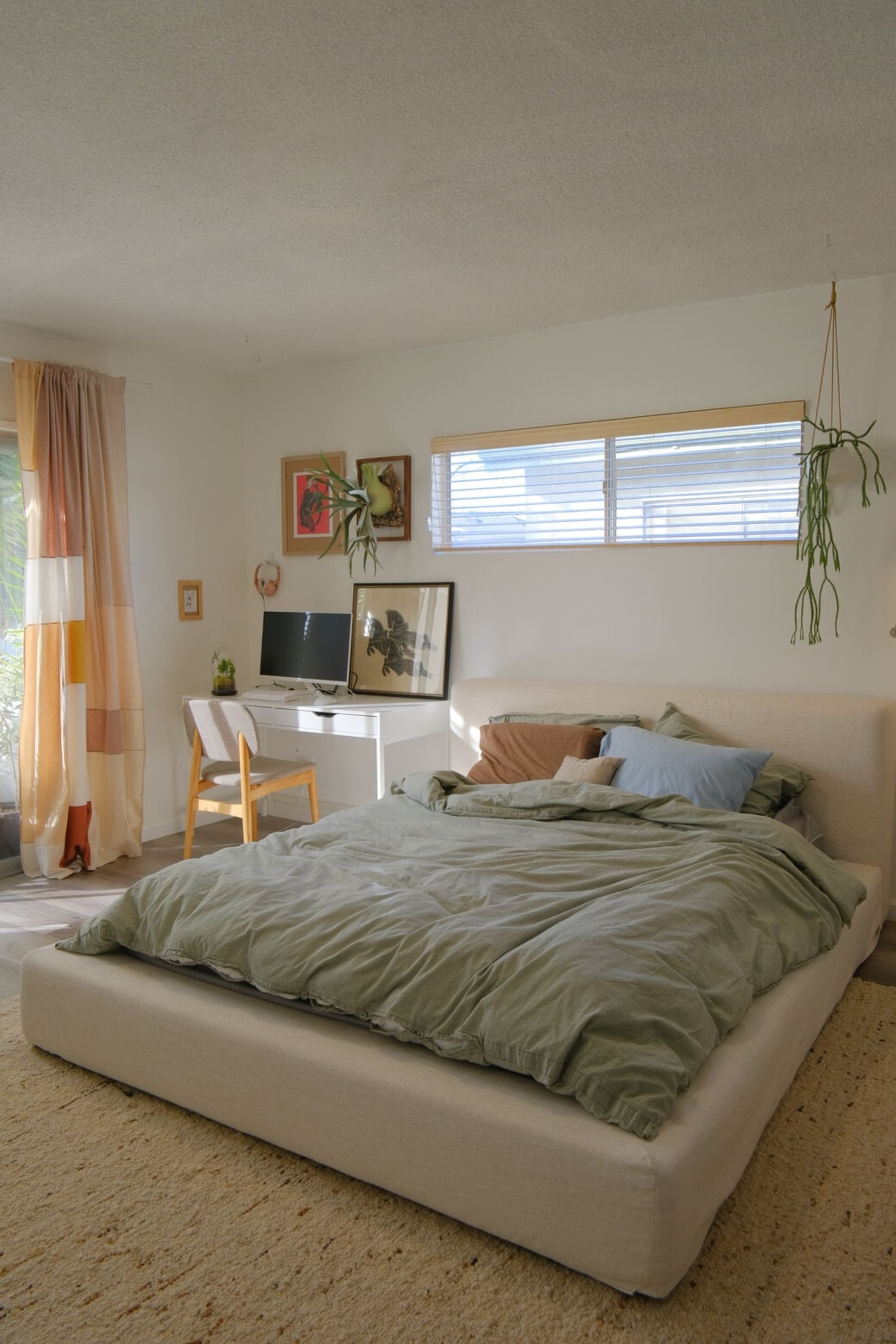 A platform bed with a sage green bedding and cushions