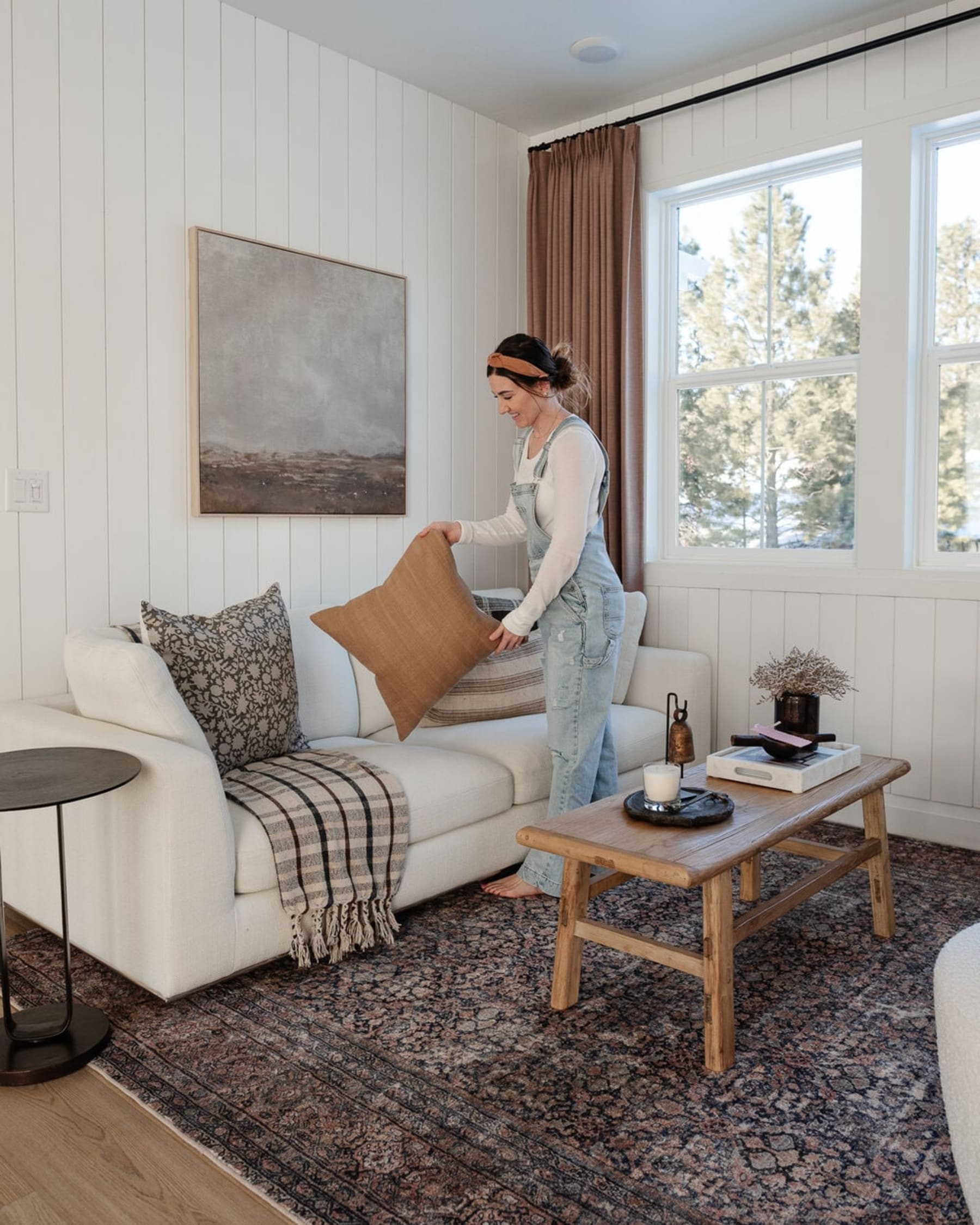 A person is placing accent pillows on a white fabric sofa.