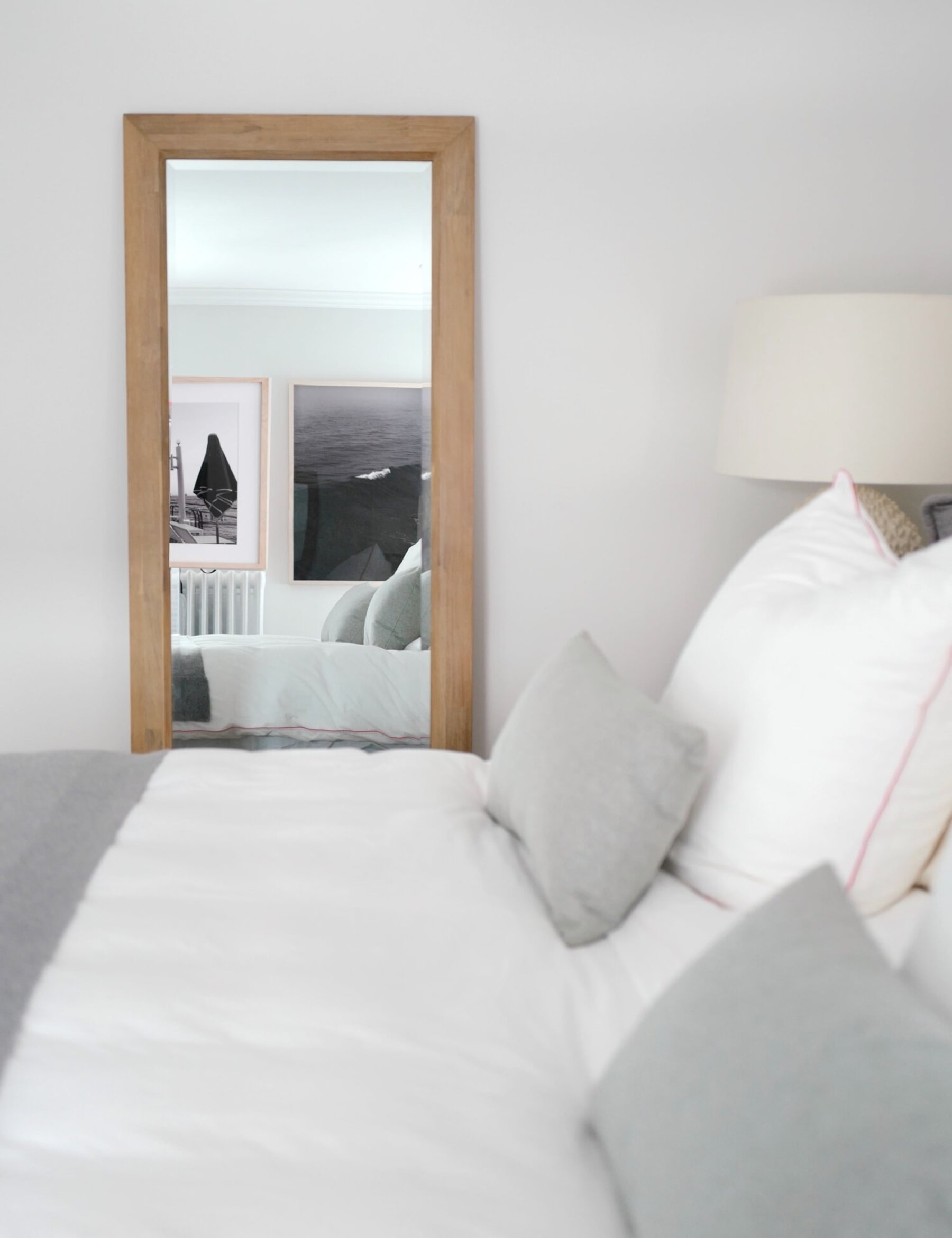 A wooden-framed mirror is placed beside a bed.